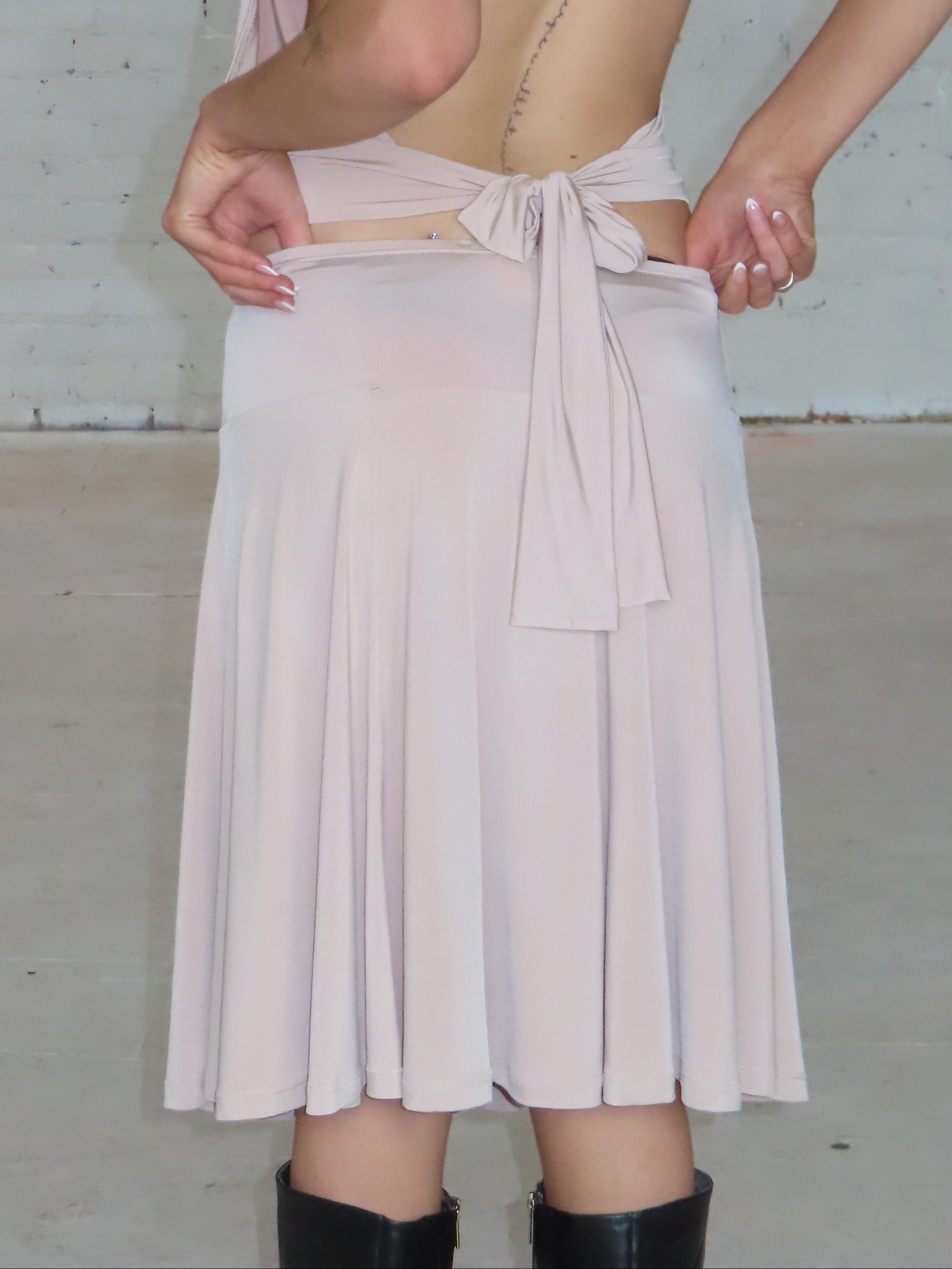 Person wearing a beige dress with a pleated skirt against a plain background