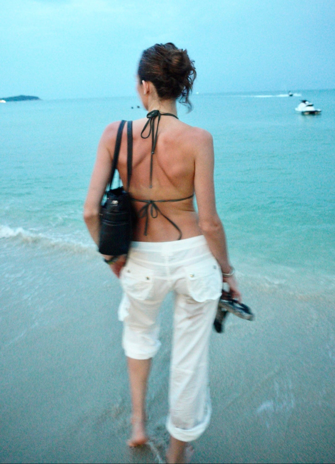 Woman walking on a beach with a black bag and white cotton cargo pants from sabi the label